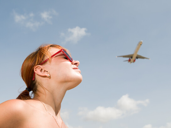 Young woman watching an airplane in the sky, feeling a sense of longing