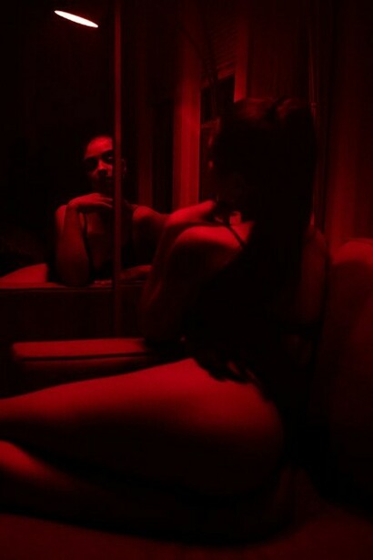 In a room bathed in dark red light, a woman poses in her underwear