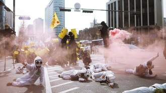 Protesters in scrub suits lie on the road surrounded by smoke during an anti-nuclear demonstration