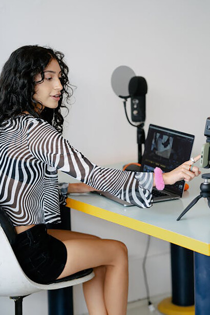 A woman seated at a desk surrounded by recording equipment, creating content for her social media platform
