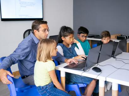 Multiethnic pupils doing task with help of teacher