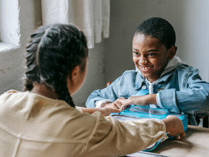 Happy Black schoolboy sharing lunch with a friend, enjoying a colorful kids’ lunchbox