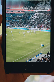 Persona mirando un partido de fútbol a través de su teléfono móvil