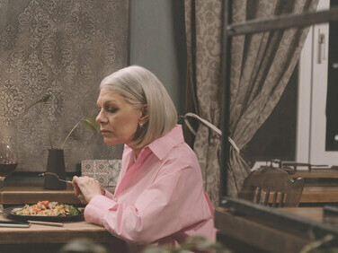 A woman in a pink long-sleeve top eating dinner alone, embodying solitude and isolation