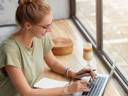 Young woman with glasses sitting in a café, working on her laptop while using an AI writing assistant