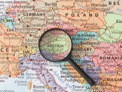 The map under the magnifying glass represents the individual EU member states, highlighting the challenge of achieving "supranational implementation" for a unified army over intergovernmental approaches
