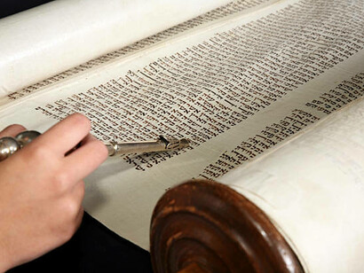 A human hand holding a yad points to the Hebrew text
