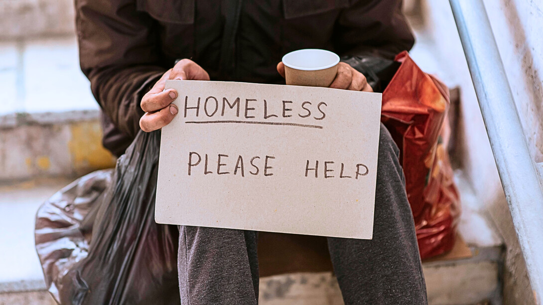 A person holding a sign stating homelessness, representing the failure of institutions to ensure safe and dignified housing