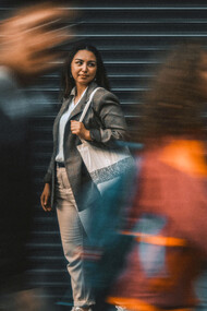Pedestrians blur past a still woman standing on the street—embodying the tension between speed and stillness in an accelerated world