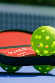 A pickleball paddle with four pickleballs, ready for a game on a sunny court