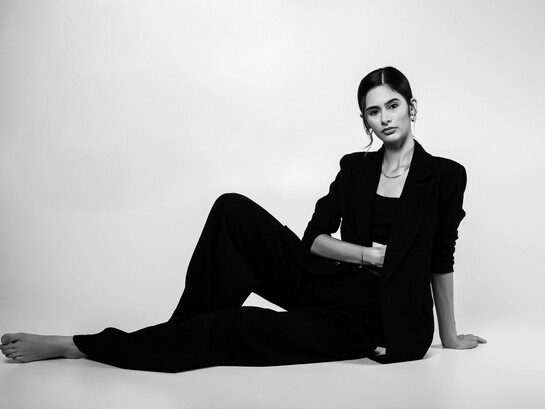 A portrait of a female model posing confidently in a studio, dressed in a sleek black suit that embodies modern sophistication and timeless style