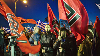 A photo of Golden Dawn members holding flags featuring the meander symbol during a rally outside the party headquarters in Athens, March 2015