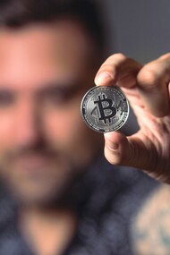Pessoa segurando uma moeda Bitcoin prateada