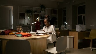 A young African American fashion designer working late in her sewing workspace, a creative professional deep in thought