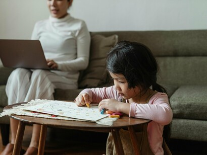 Criança desenha livremente enquanto a mãe trabalha no computador. Resgatar a infância é um ato político. É dizer não à lógica do capital que exige aceleração constante e rendimento a todo custo. É afirmar que o brincar é um direito, não um luxo reservado a poucos. É defender que a escola seja um território de acolhimento, de escuta sensível e de produção de sentido, e não uma máquina de normatização. É sustentar que a diferença não é um problema a ser corrigido, mas uma riqueza a ser cultivada e respeitada