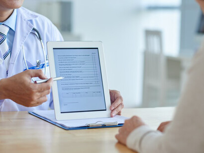 A healthcare professional using a digital tablet to assess and discuss a patient's medical diagnosis and treatment plan