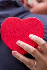 A woman embraces a man while holding a heart-shaped gift box