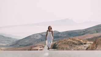 A woman walking on a road near hills under a cloudy sky, smiling, symbolizing her healing journey, spiritual warfare, and overcoming trauma, embodying peace and purpose