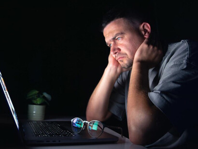 A young man sits at his computer at night, visibly upset