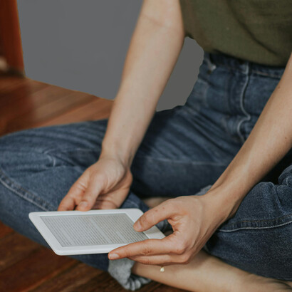 Someone sits on a wooden deck, immersed in reading an e-book