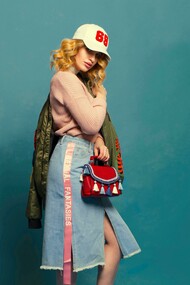 Foto de mulher vestindo saia jeans, agasalho de lã com uma jaqueta verde musgo e um boné branco