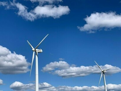 Two Micon wind turbines stand against a bright blue sky dotted with fluffy white clouds, illustrating the growing prominence and visual presence of wind energy technology 