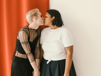 A woman in a black dress and a woman in a white shirt sharing a kiss