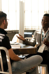 Two men engage in a deep conversation, pondering the complexities of merit and achievement, as they navigate the challenges of imposter syndrome and the deserving threshold