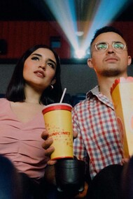 A couple at the cinema have their popcorn and drinks and are eagerly anticipating the movie they are about to watch