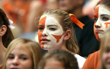 Blonde woman with orange and white face paint watching a football match