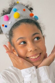 Menina negra feliz com coroa colorida com pompoms