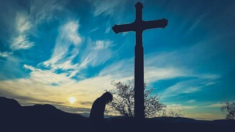 A person kneeling before a cross on a hill, representing a return to sincere and humble faith